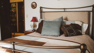 Una cama bien hecha con cabecera de madera, una mesita de noche con lámpara y una estantería al fondo.
