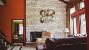 A living room with a fireplace, a sofa, and a chair. - Shane Acres Country Inn (Juneau)