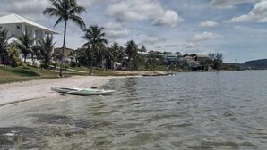 Une plage avec une eau claire, un bateau et des maisons en arrière-plan.