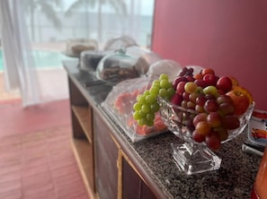 Un mostrador de buffet amb diverses fruites i un bol de vidre ple de raïm, pomes i talls de meló.