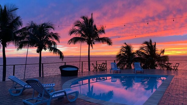 Une piscine avec des chaises longues, des palmiers et une vue imprenable sur le coucher de soleil.