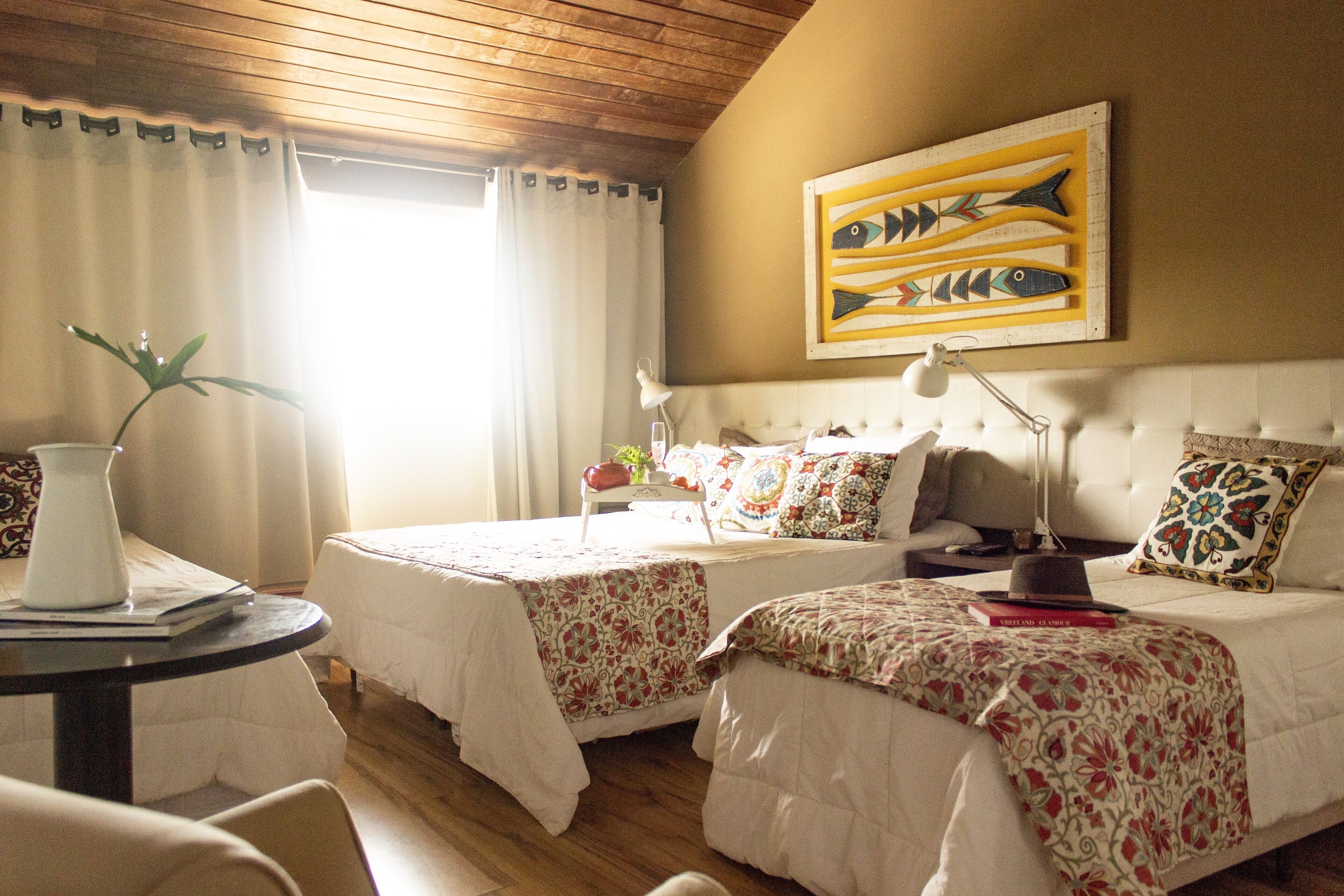 Een hotelkamer met twee bedden, een tafel met een vaas en een vis schilderij aan de muur.