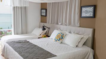 A bedroom with a large bed, a bedside lamp, and a view of the sea.