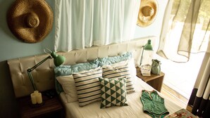 Un dormitorio ordenado con cama, almohadas, una mesita de noche, lámpara y ventana con cortinas.