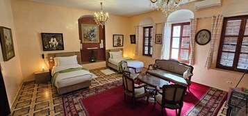 Habitación de hotel con dos camas, una mesa de comedor con sillas, una araña y obras de arte en las paredes.