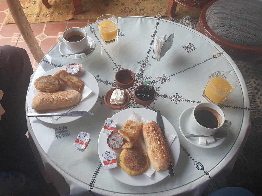 A round table with a white tablecloth, plates of food, cups of coffee, and a glass of orange juice.