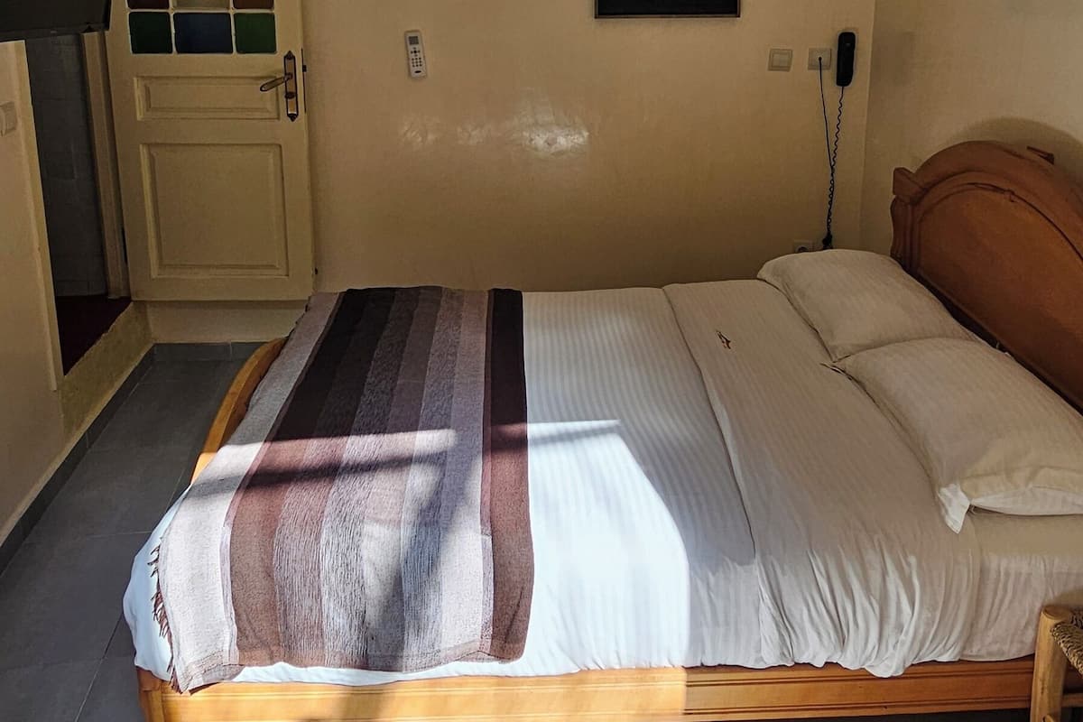 Un dormitorio con cama, puerta con ventana, aire acondicionado y teléfono fijo en la pared.