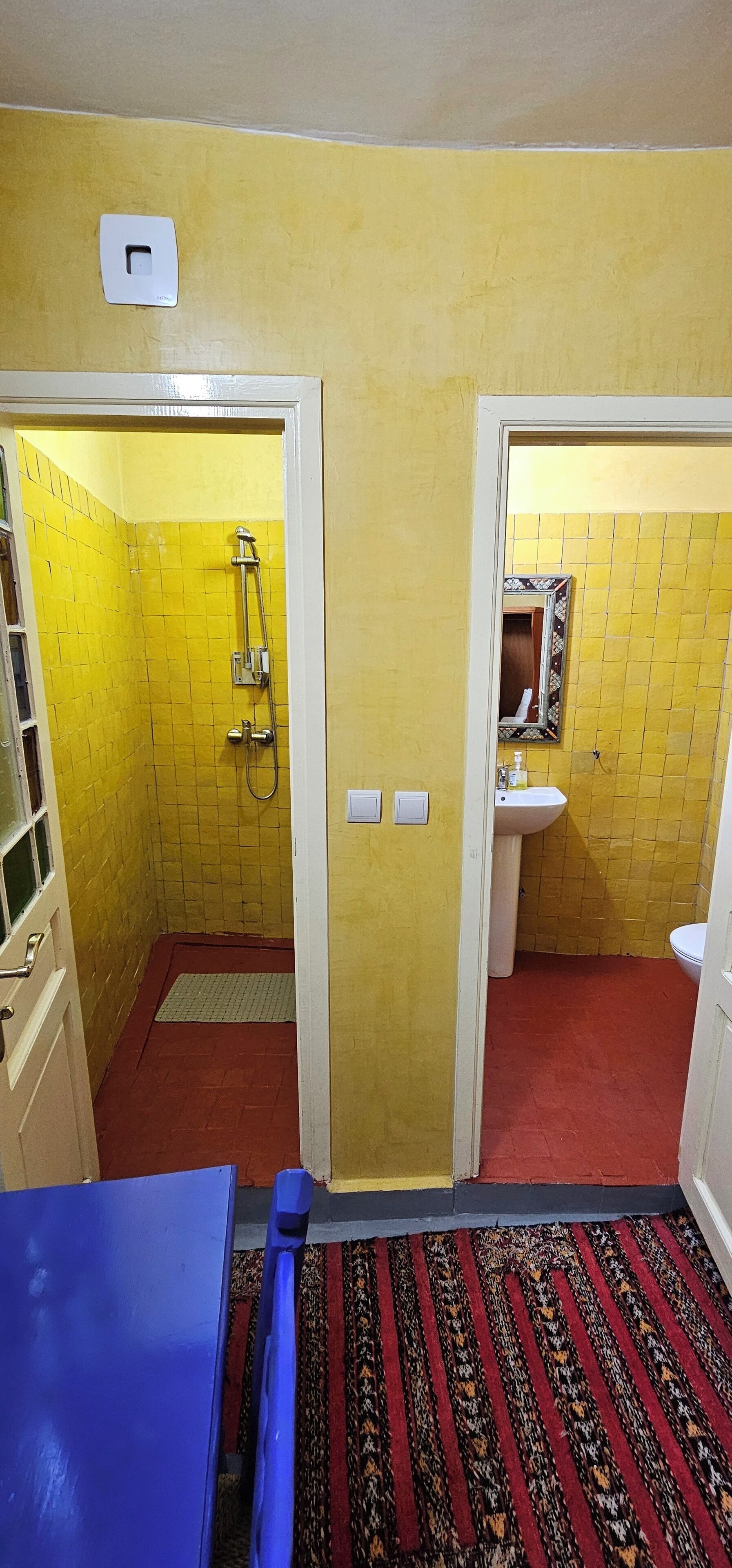 Une salle de bain avec des murs recouverts de carreaux jaunes, une douche, un lavabo et un miroir.