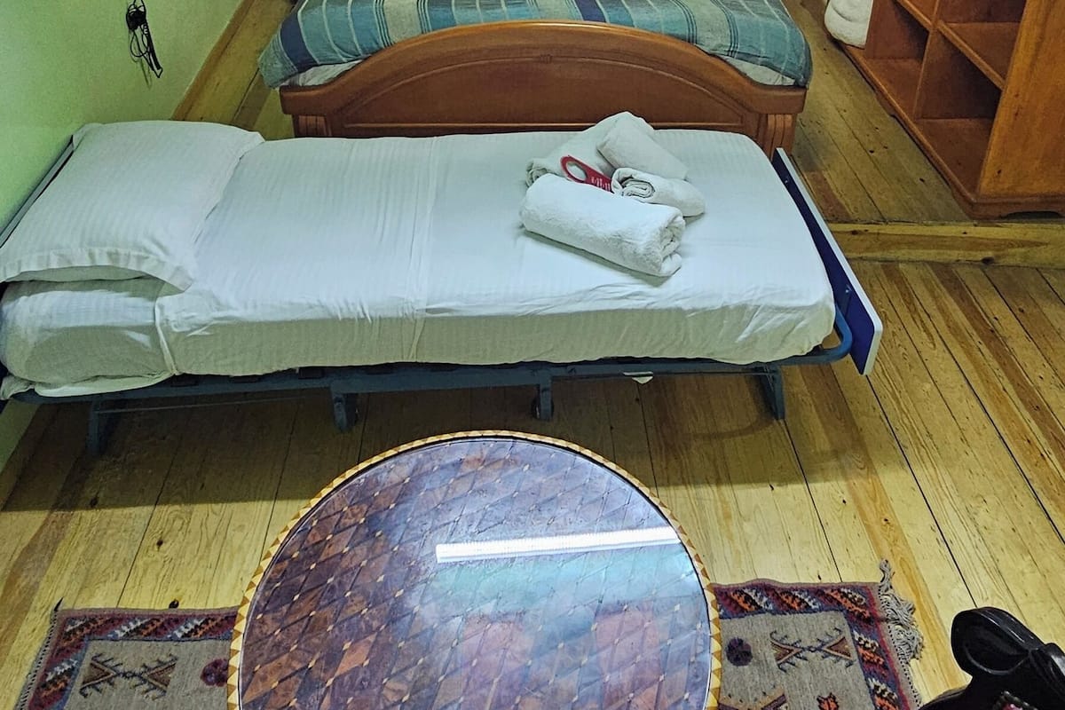 Una habitación con dos camas, una mesita redonda pequeña y un armario de madera.
