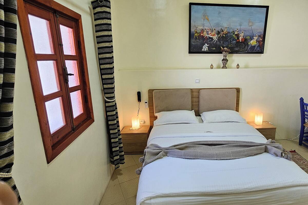 Un dormitorio con cama, lámparas de noche, un escritorio y una silla.
