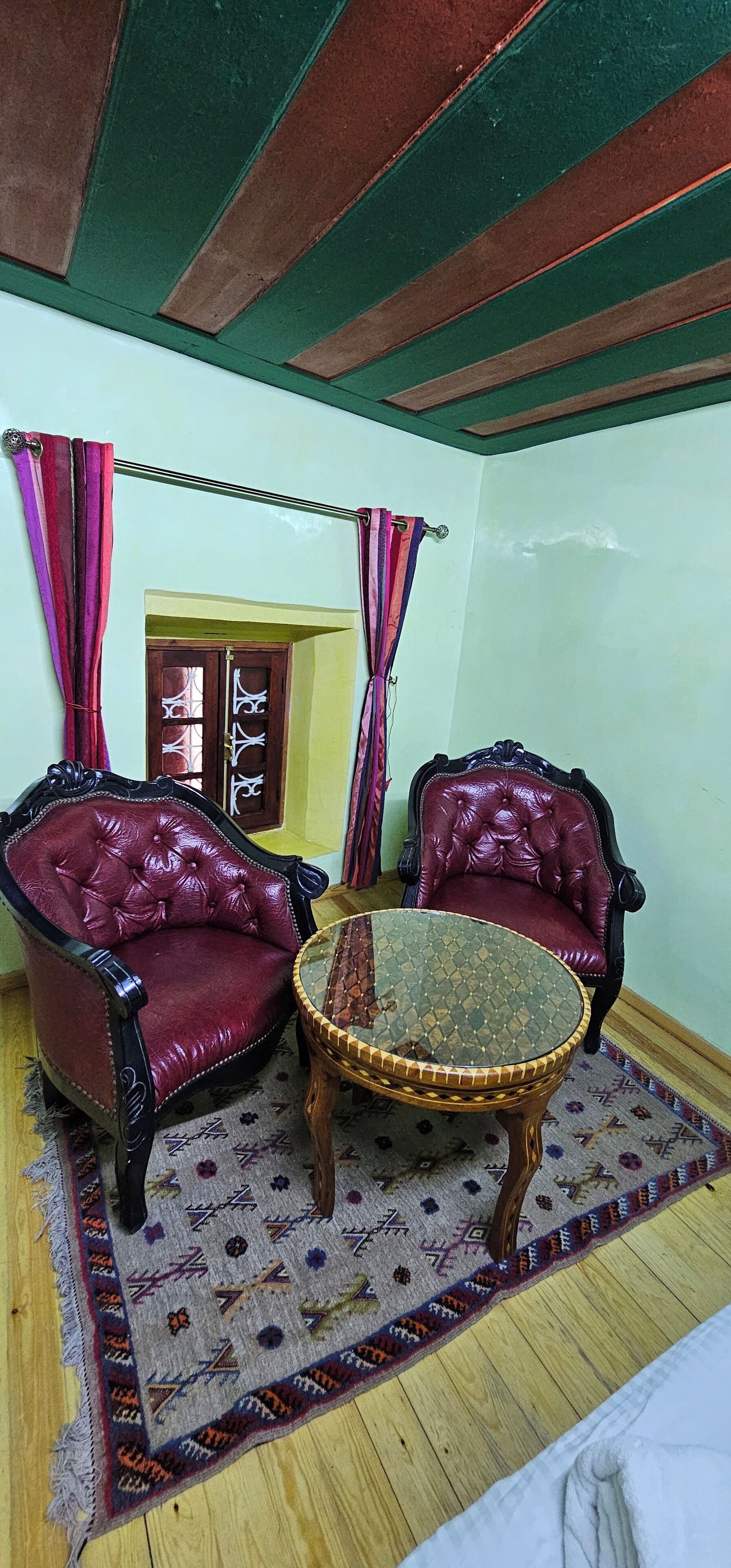 Une pièce comprenant deux fauteuils en cuir rouge, une table avec un plateau en verre, un tapis à motifs et un plancher en bois.