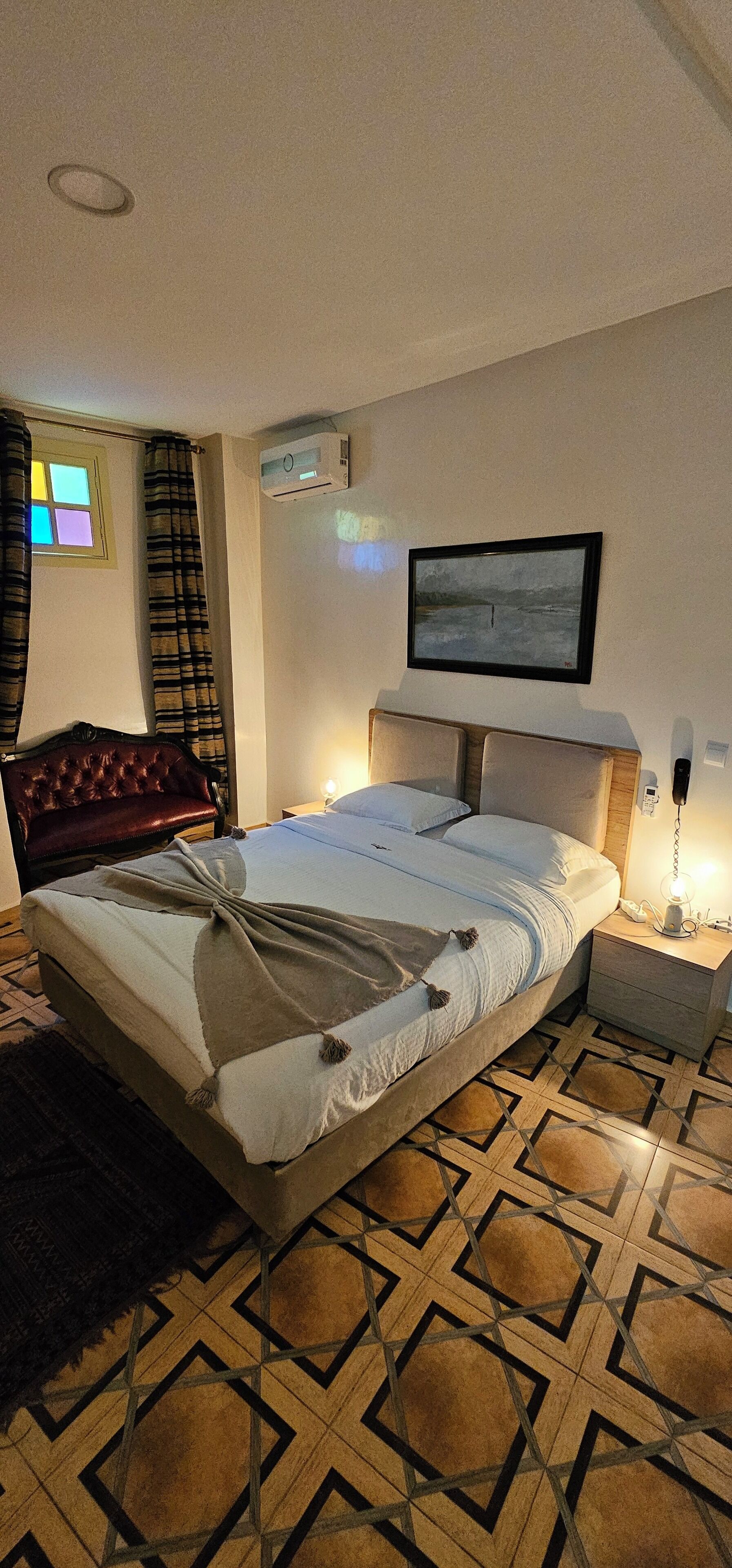 A hotel room with a bed, a chair, a TV, and a nightstand with a lamp.