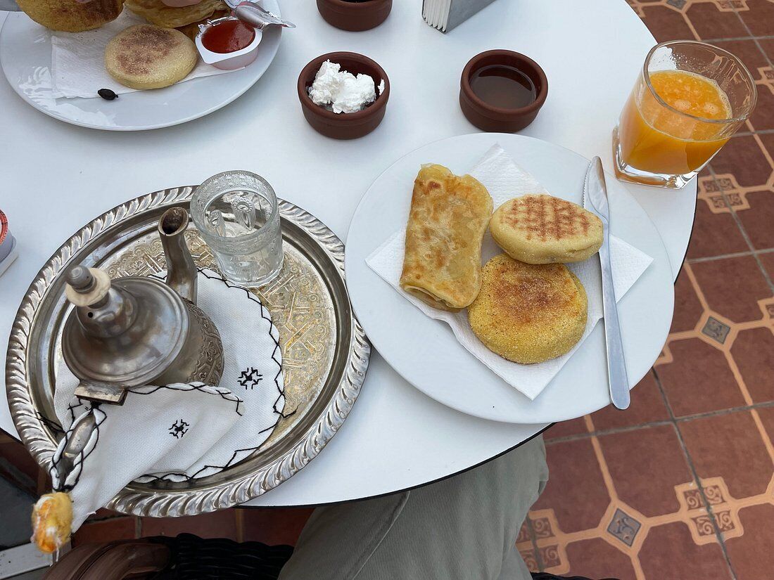 A table with a tray of food, including pastries and a teapot, and a glass of orange juice.