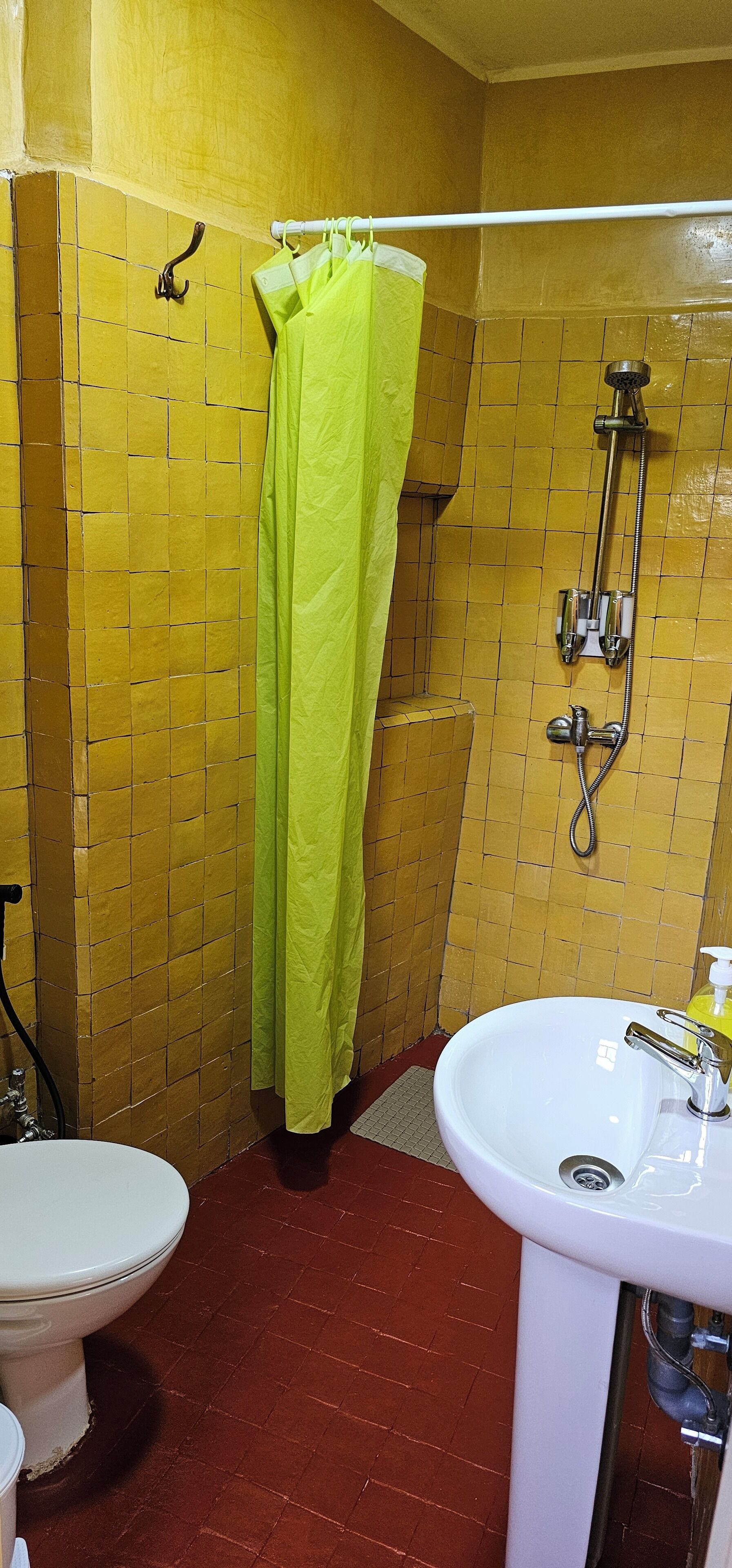 A bathroom with yellow tiled walls, a green shower curtain, a white sink, and a toilet.