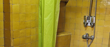 A bathroom with yellow tiled walls, a green shower curtain, a white sink, and a toilet.