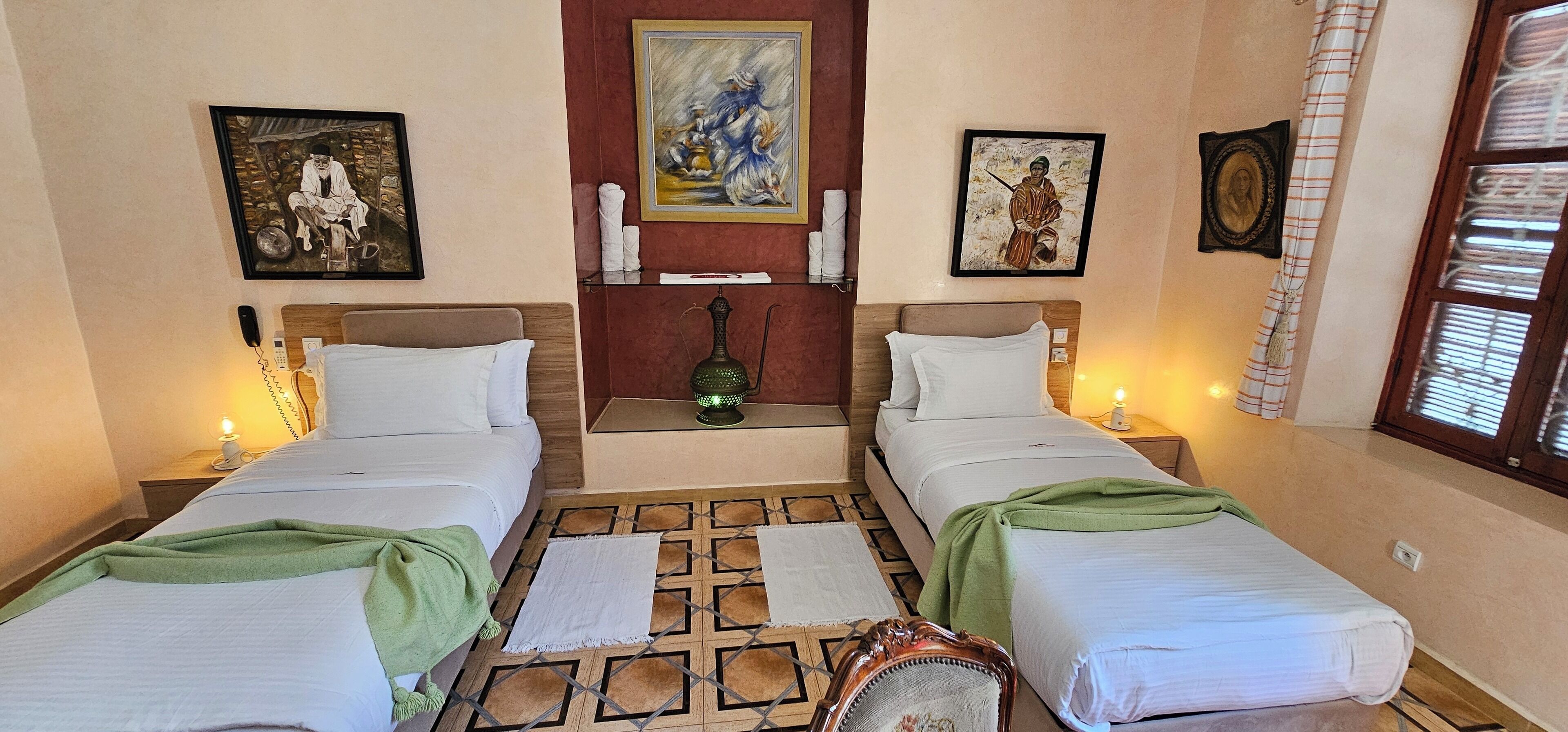 Habitación de hotel con dos camas, una mesita con un florero y obras de arte en las paredes.