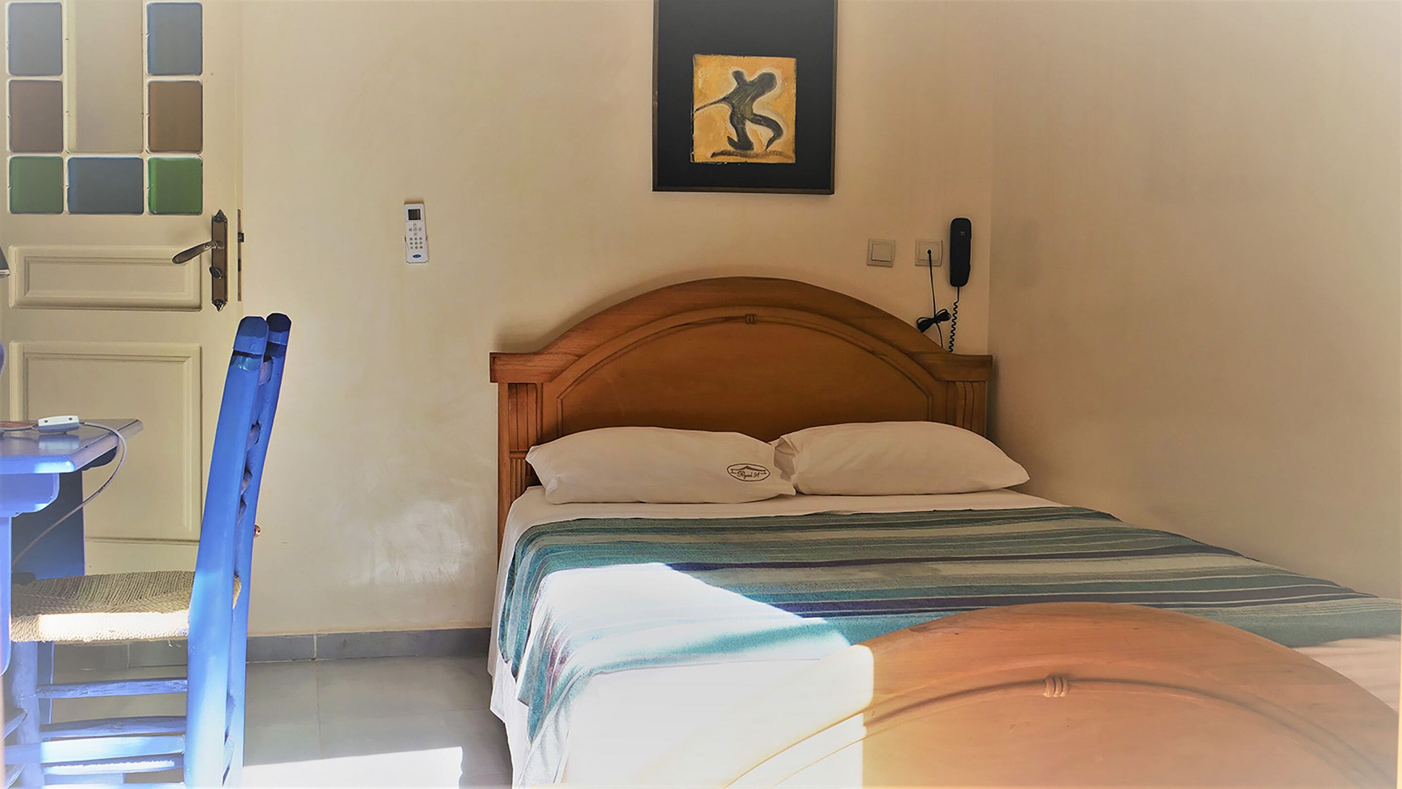A room with a bed, a chair, a desk, a phone, and a painting on the wall.
