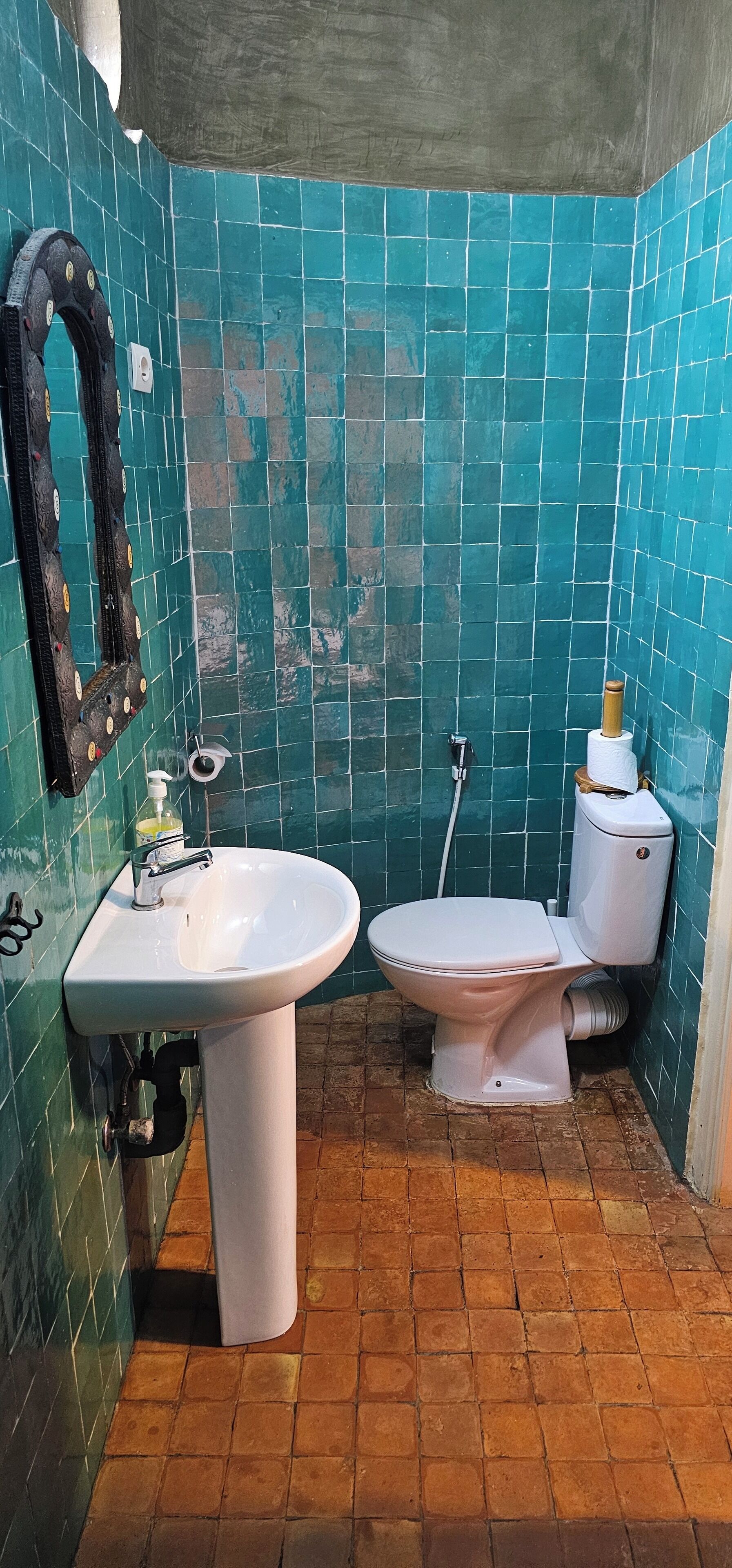 A bathroom with a white sink, toilet, and a mirror. The walls are tiled in blue, and the floor is tiled in brown.