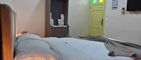 A bedroom with a bed, bedside table with a lamp, a wardrobe, a green door, and a television on the wall.