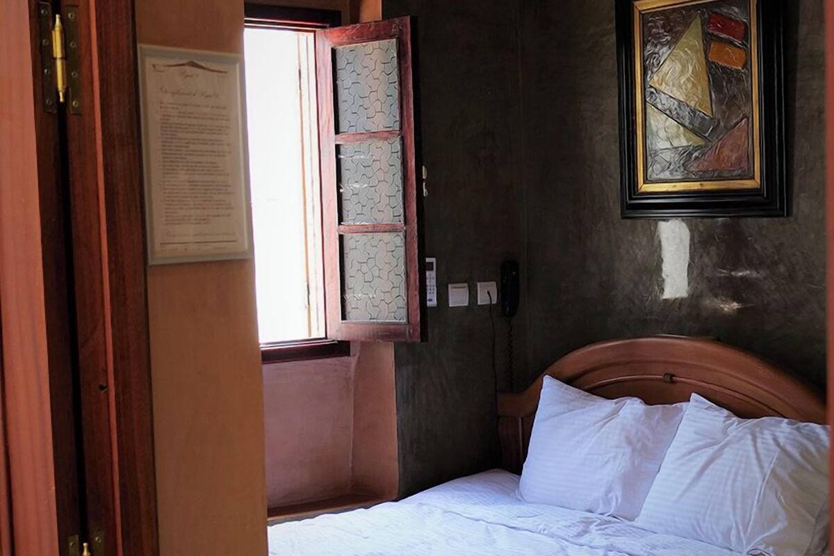 Un dormitorio con cama, ventana con vistas, una obra de arte enmarcada en la pared y una puerta con marco de madera.