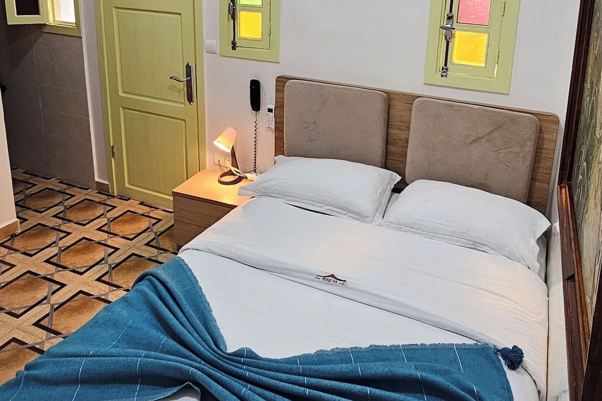 Un dormitorio con cama, mesita de noche, teléfono y una puerta con vidrieras de colores.
