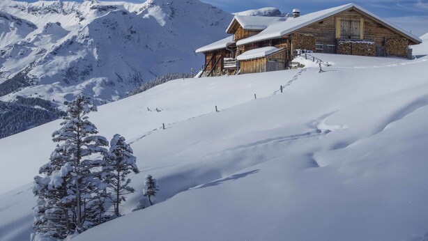 Un chalet en bois situé sur une pente enneigée d’une montagne, sous un ciel dégagé.