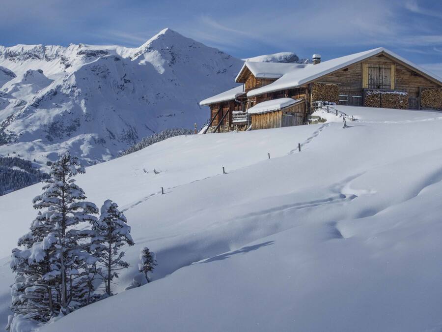 A wooden lodge on a snowy mountain slope with a clear sky.