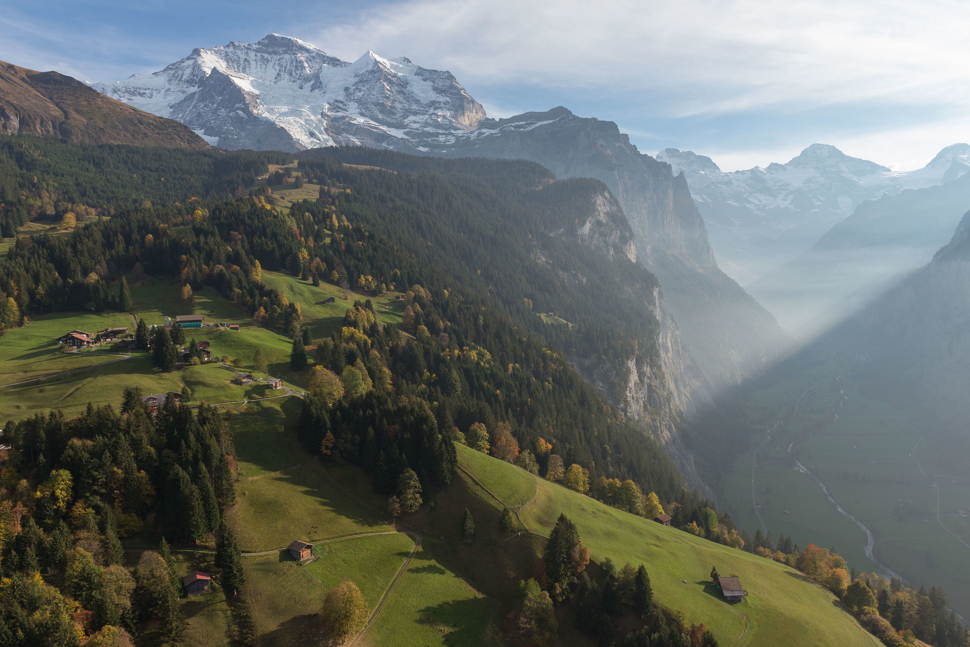 A mountainous landscape with a valley, houses, and a prominent snow-capped peak.