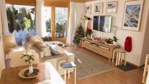 Un salon chaleureux avec un canapé, une table basse, une petite table à manger et un téléviseur. On y trouve également un sapin de Noël et une cheminée.