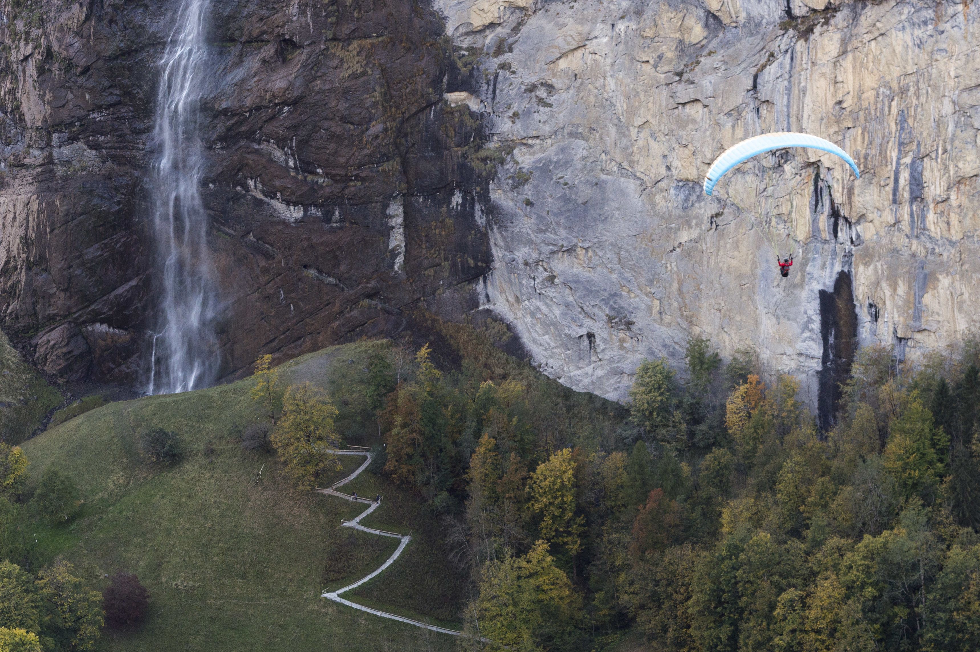 A cliffside with a waterfall and a person paragliding.