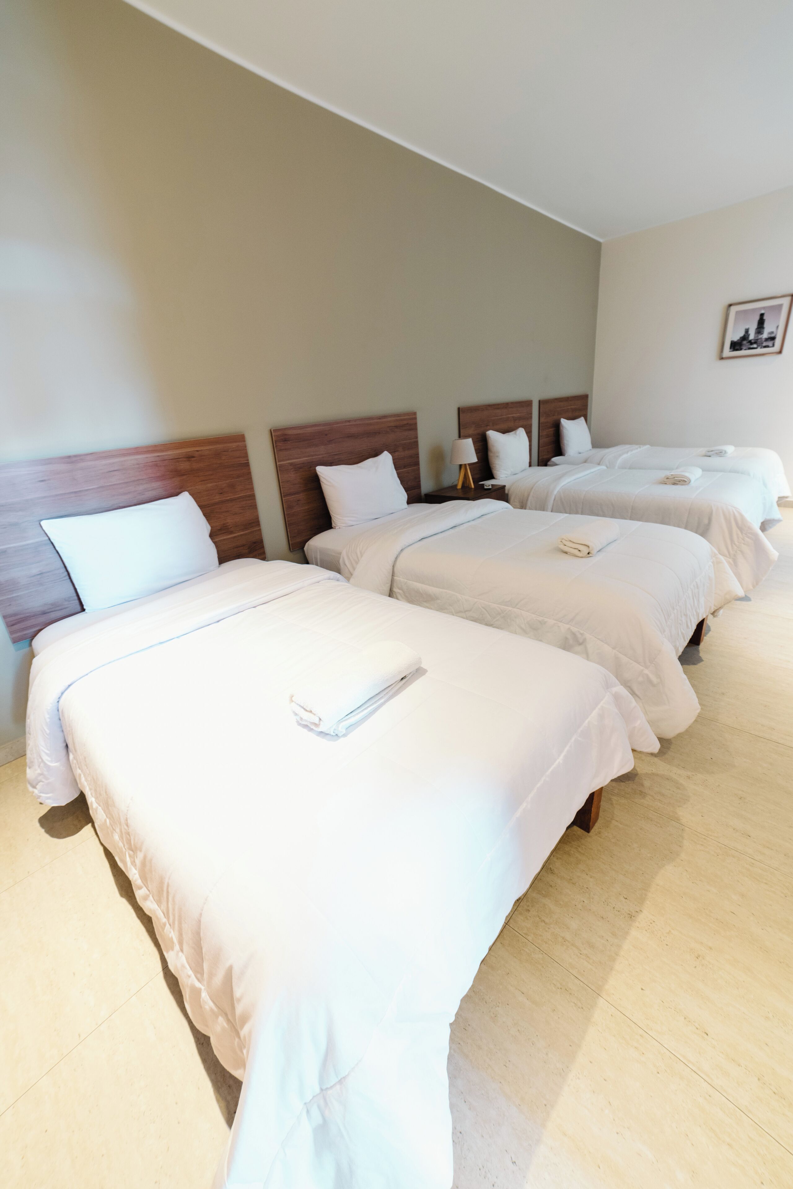 Una camera d'albergo con tre letti rifatti, ognuno con lenzuola e cuscini bianchi.