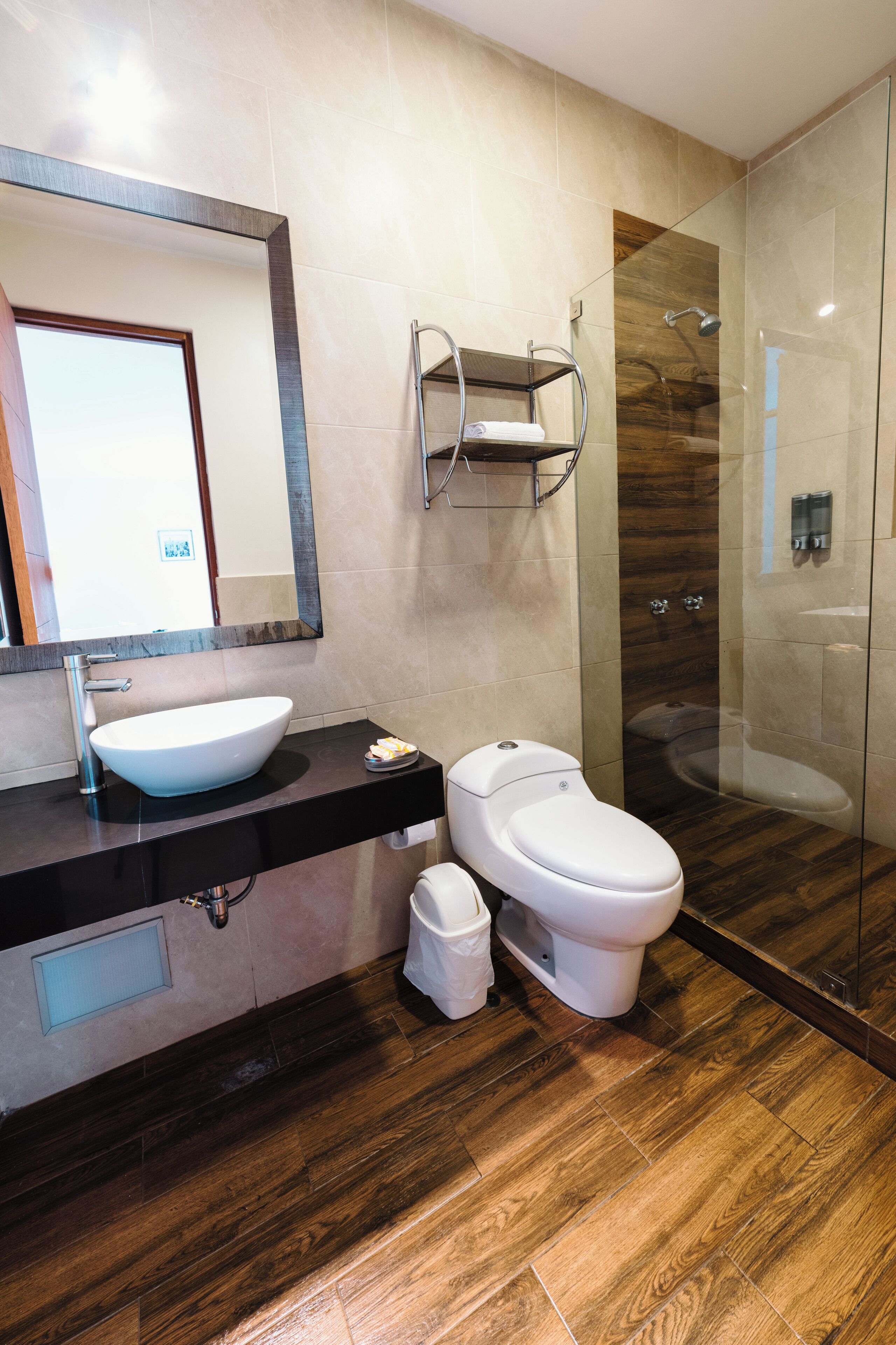Un baño moderno con un espejo grande, un lavamanos blanco, un inodoro y una zona de ducha con mampara de cristal.