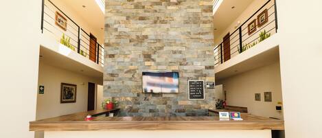 A reception desk with a stone wall backdrop, a flat-screen TV, and a sign with check-in/out times.