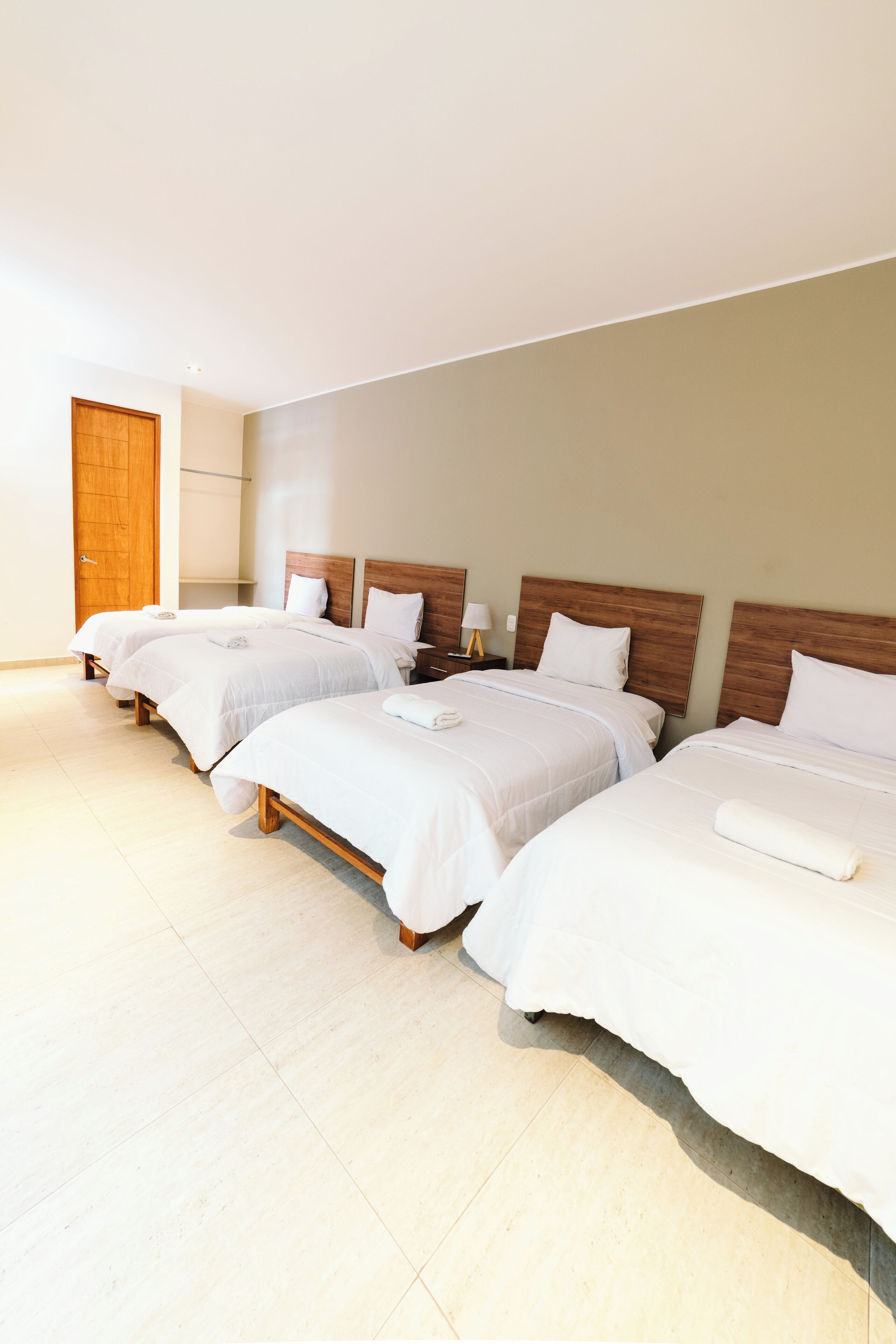 A hotel room with three beds, wooden headboards, white bedding, and a wooden door.