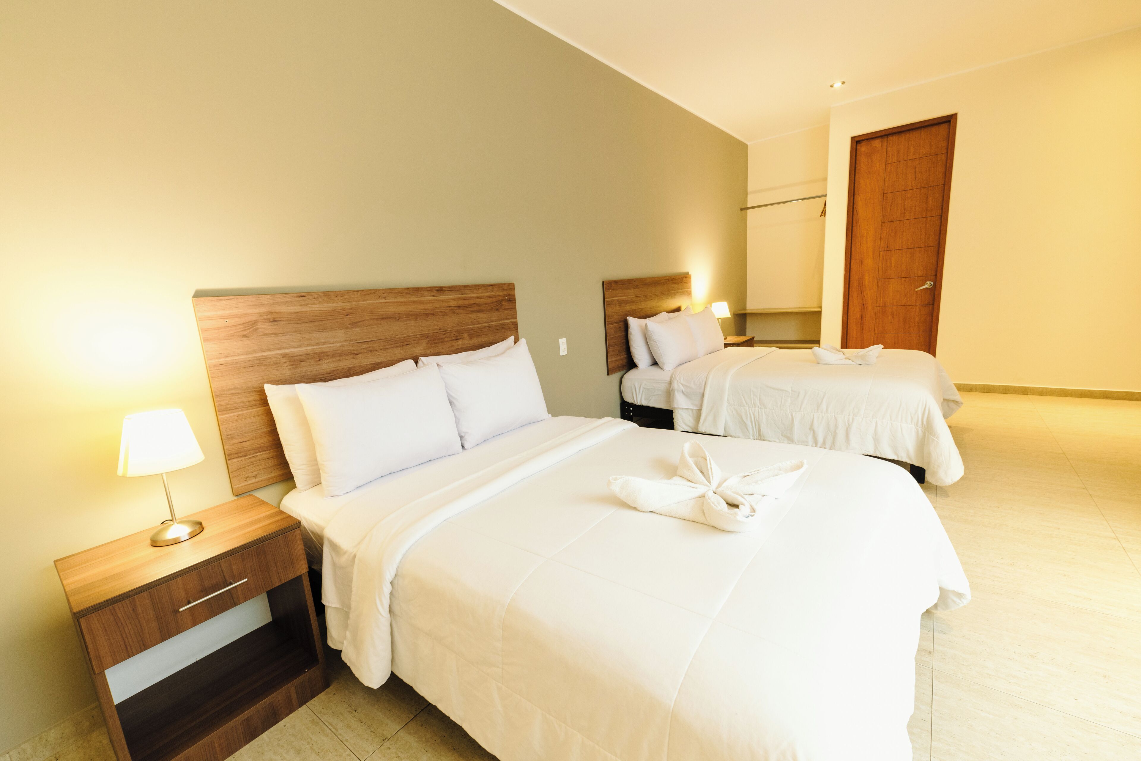 Habitación de hotel con dos camas, cabeceros de madera, ropa de cama blanca y lámparas de noche.