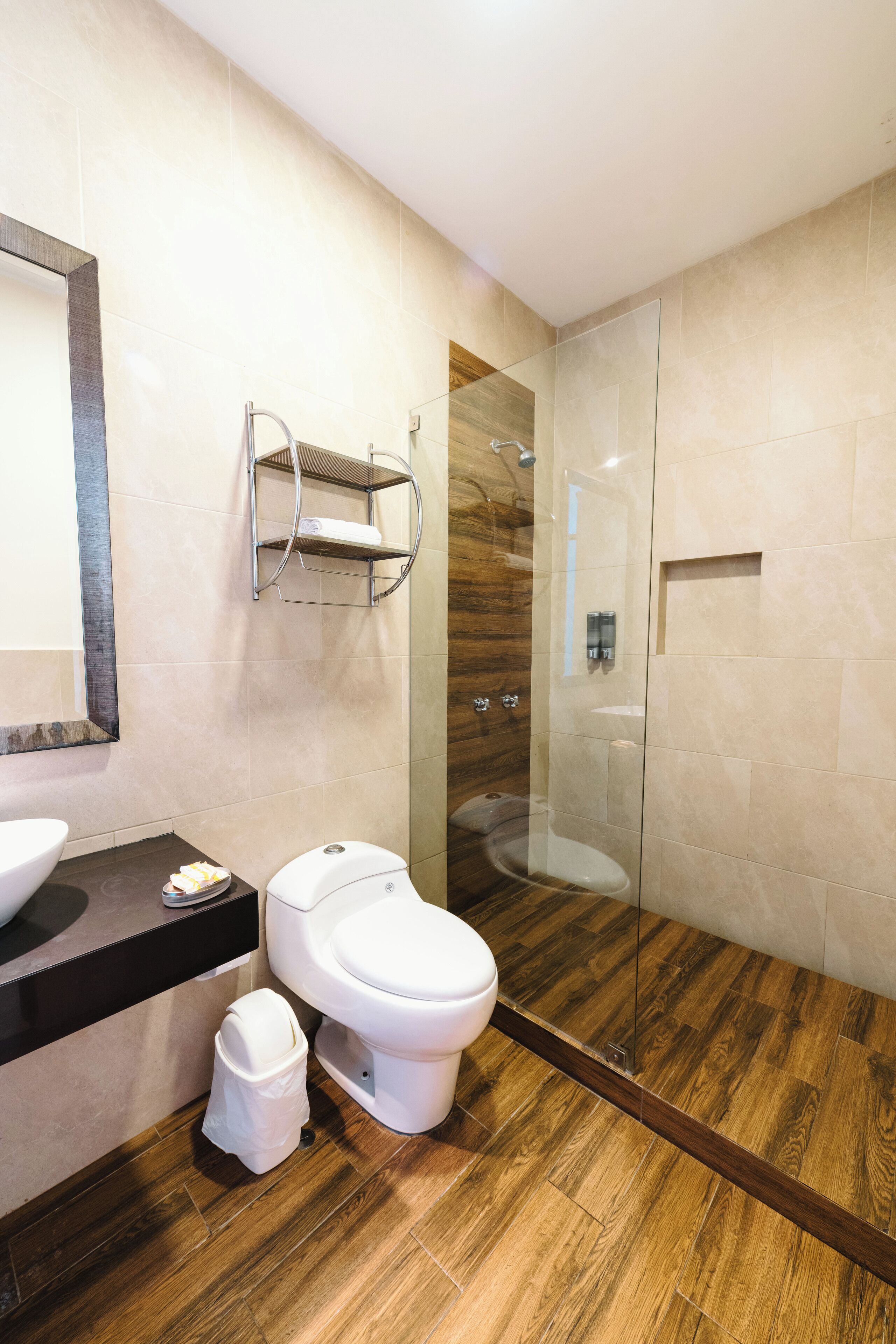 Ein modernes Badezimmer mit Holzboden, einer Duschkabine aus Glas, einer weißen Toilette und einem Waschbecken mit Spiegel darüber.