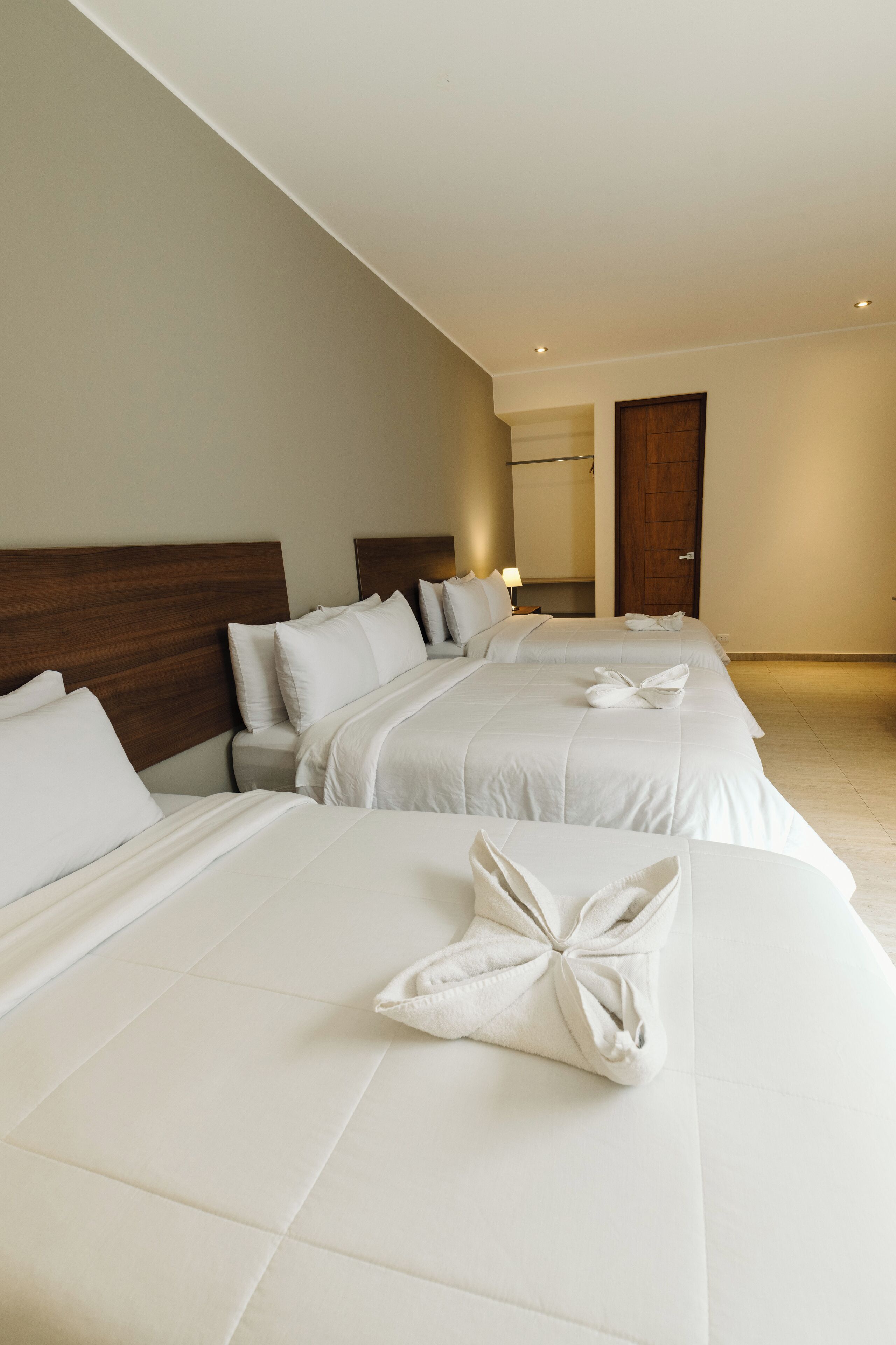 A hotel room with two beds, each with white linens and pillows, a wooden headboard, and a nightstand with a lamp.