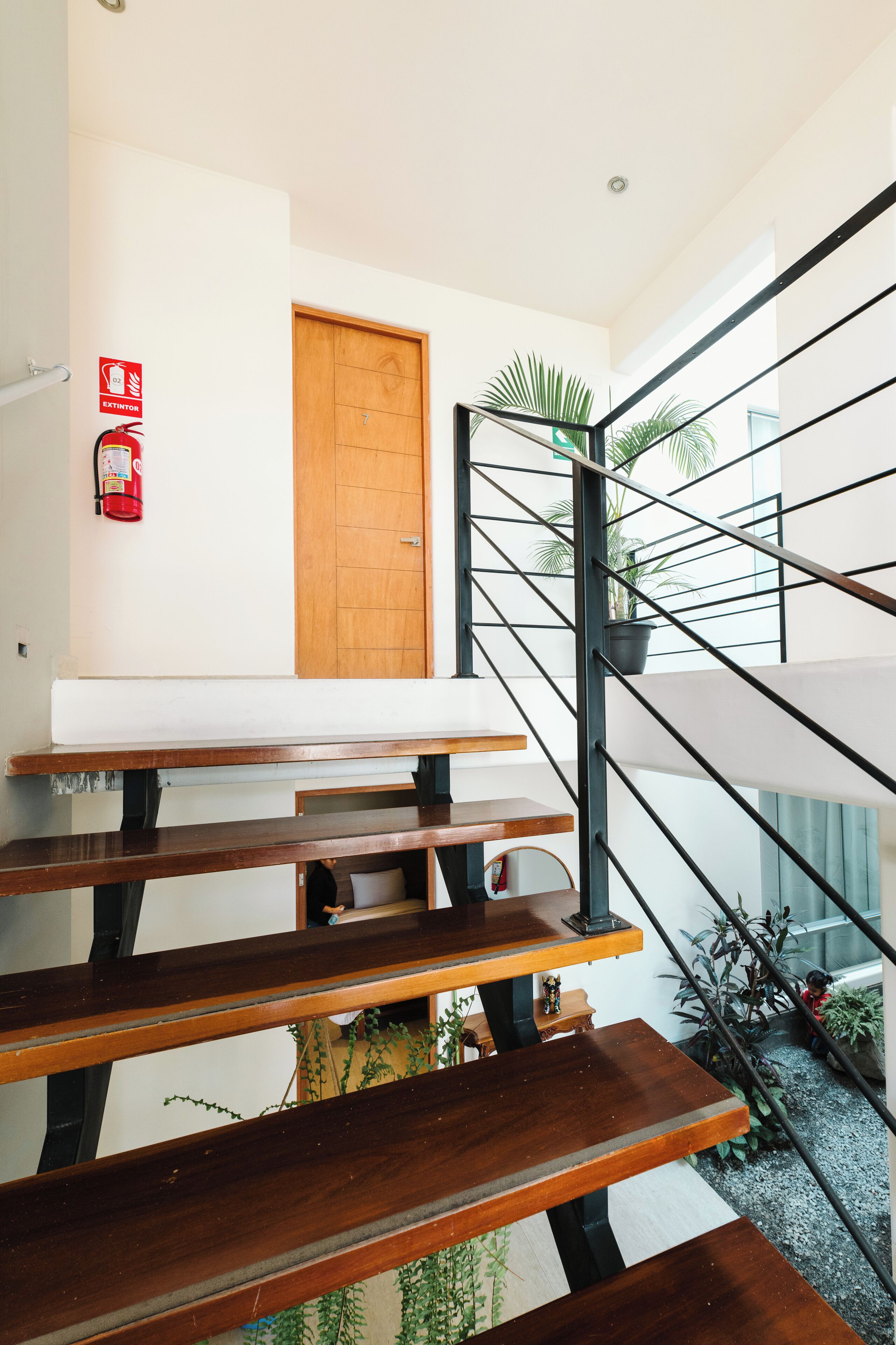 A staircase with wooden steps and metal railings, a wooden door with a number, and a fire extinguisher on the wall.