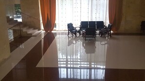 Een ruime kamer met een gepolijste vloer, een trap aan de linkerkant, en een zithoek met stoelen en een tafel in het midden.