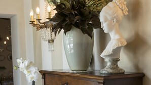 A wooden cabinet with a vase of flowers, a bust, and a candle holder. - B&B La Chiusa Delle Monache (Lucca)