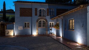 A two-story building with a central arched doorway, multiple windows, and a gravel driveway. - B&B La Chiusa Delle Monache (Lucca)