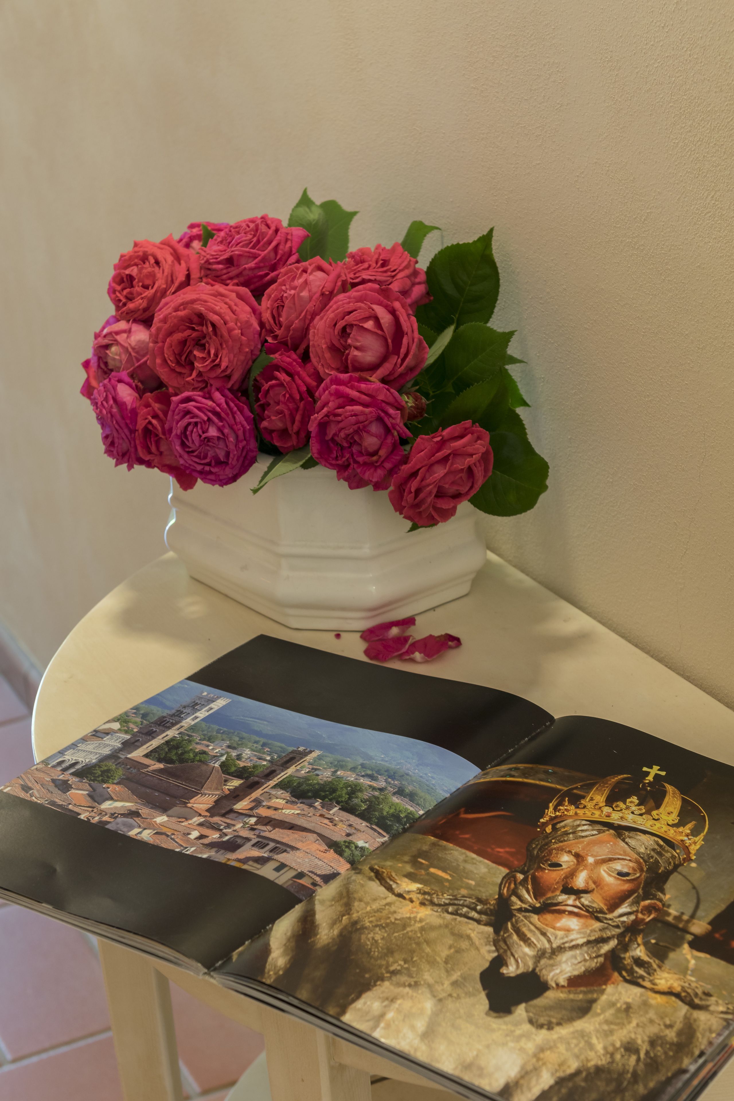 A white vase with pink roses on a white table.