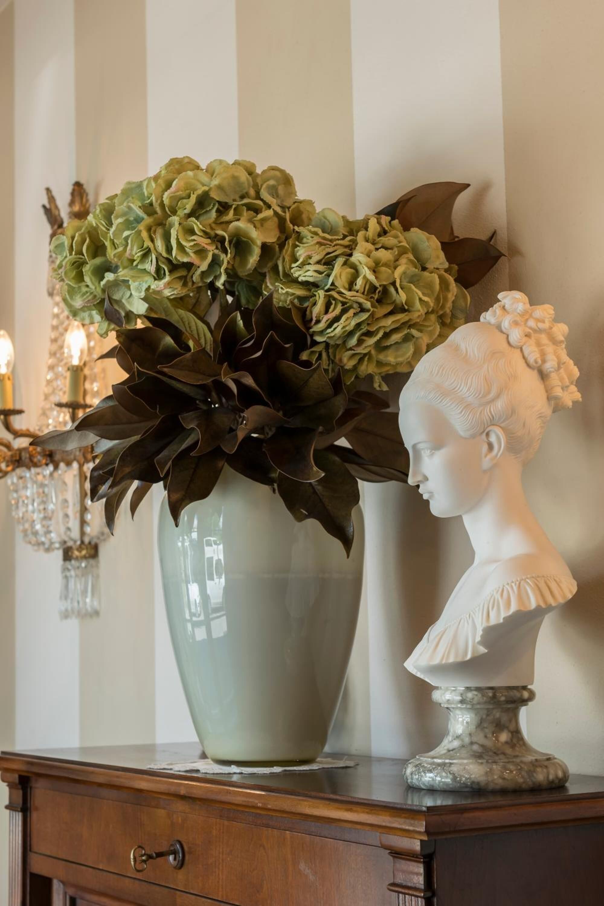 Een vaas met groen blad en een bustebeeld op een houten dressoir.