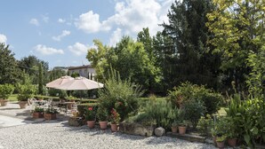 A garden patio with a table and chairs, surrounded by potted plants and a large umbrella. - B&B La Chiusa Delle Monache (Lucca)