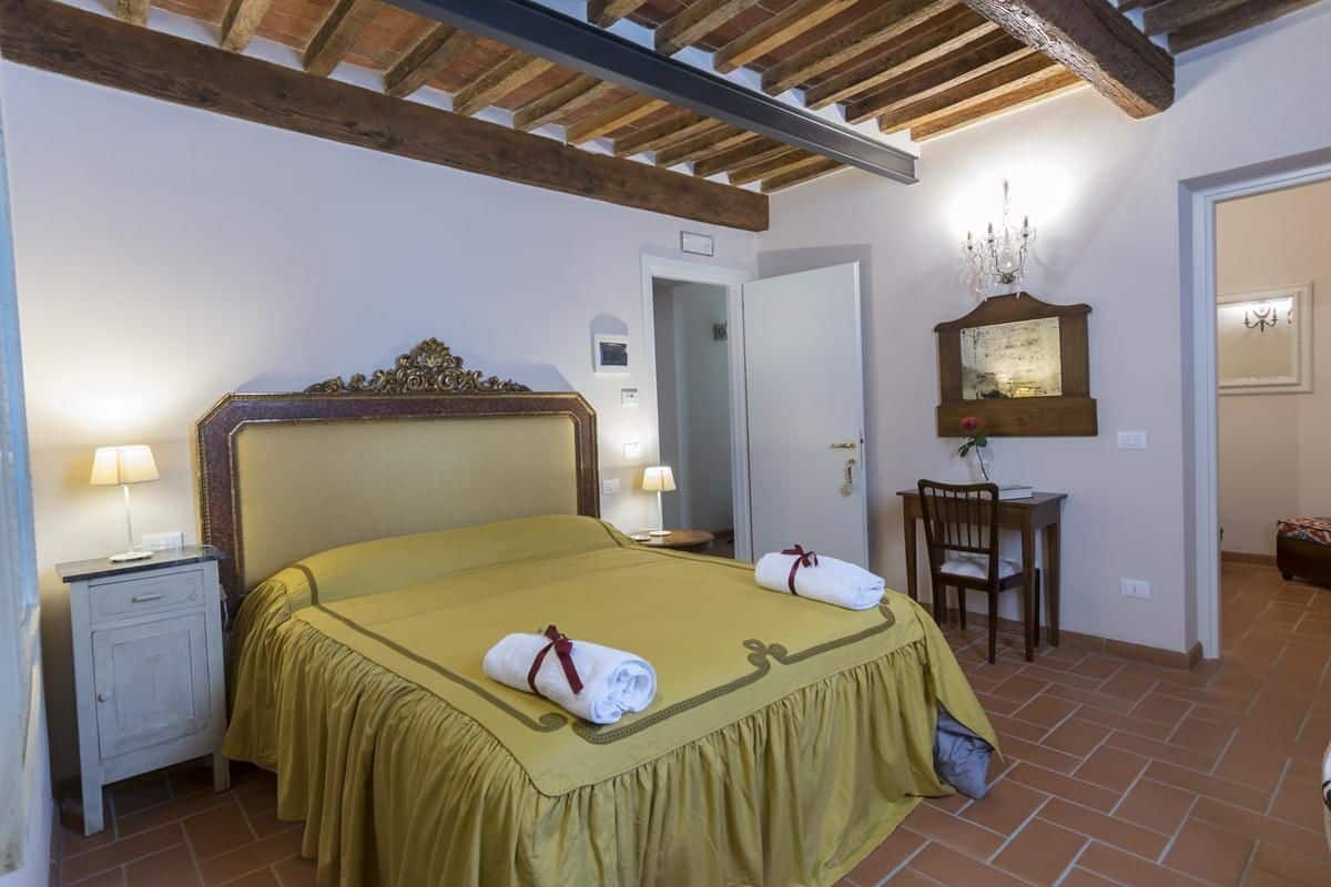 A hotel room with a bed, nightstand, chair, and a small table with a lamp.