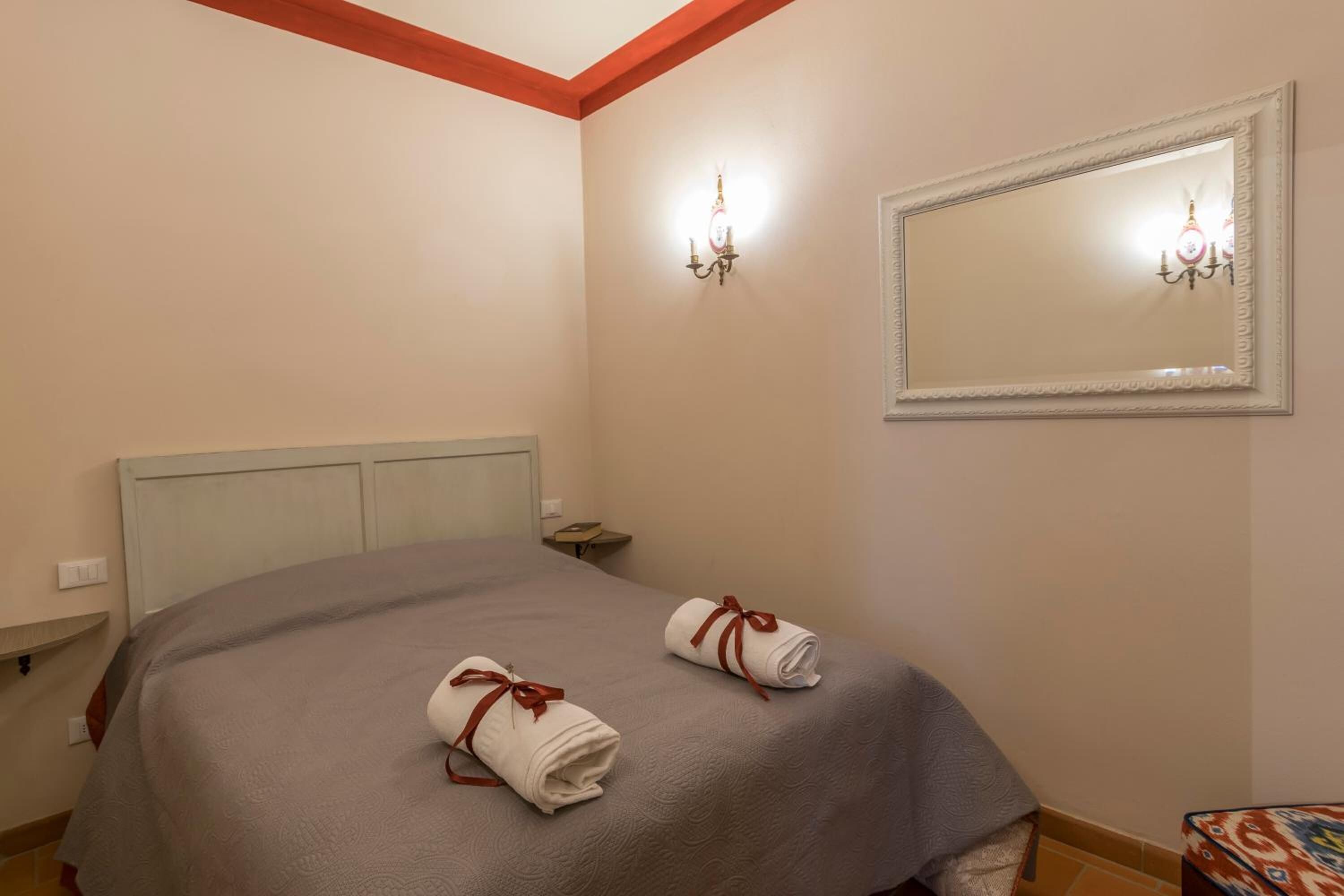 Een slaapkamer met een bed, twee handdoeken op het bed, een nachtkastje, een spiegel en een wandlamp.