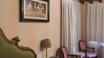 Een hotelkamer met een bed, een ingelijste foto aan de muur, een lamp, twee stoelen en een raam met gordijnen.