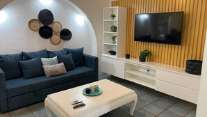 Uma sala de estar moderna com um sofá azul escuro, uma mesa de centro branca e uma TV de tela plana fixada em uma parede de madeira.