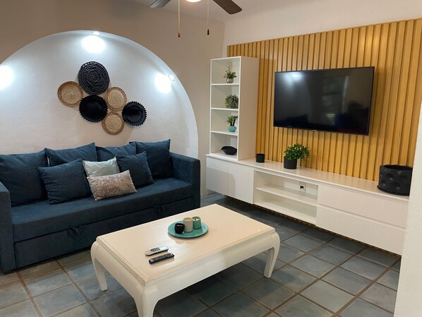 Una sala moderna con un sofá azul oscuro, una mesa de centro blanca y un televisor de pantalla plana montado en una pared de madera.