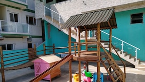 Ein Spielplatz mit einer Holzrutsche und einer Kletterkonstruktion, umgeben von einer Betonfläche.